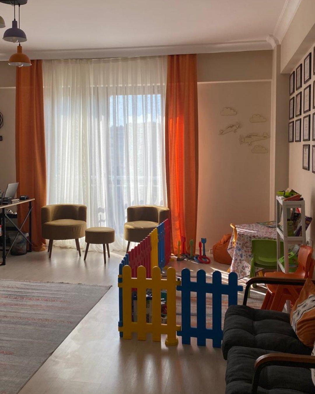 Prusa Psikoloji Bursa Nilüfer merkezinden ana oda: turuncu perdeler, oyun alanı ve rahat oturma köşesi